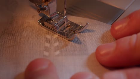 draufsicht auf nähmaschinenfuß und nadel, die sich durch den stoff und die finger des bedieners bewegen