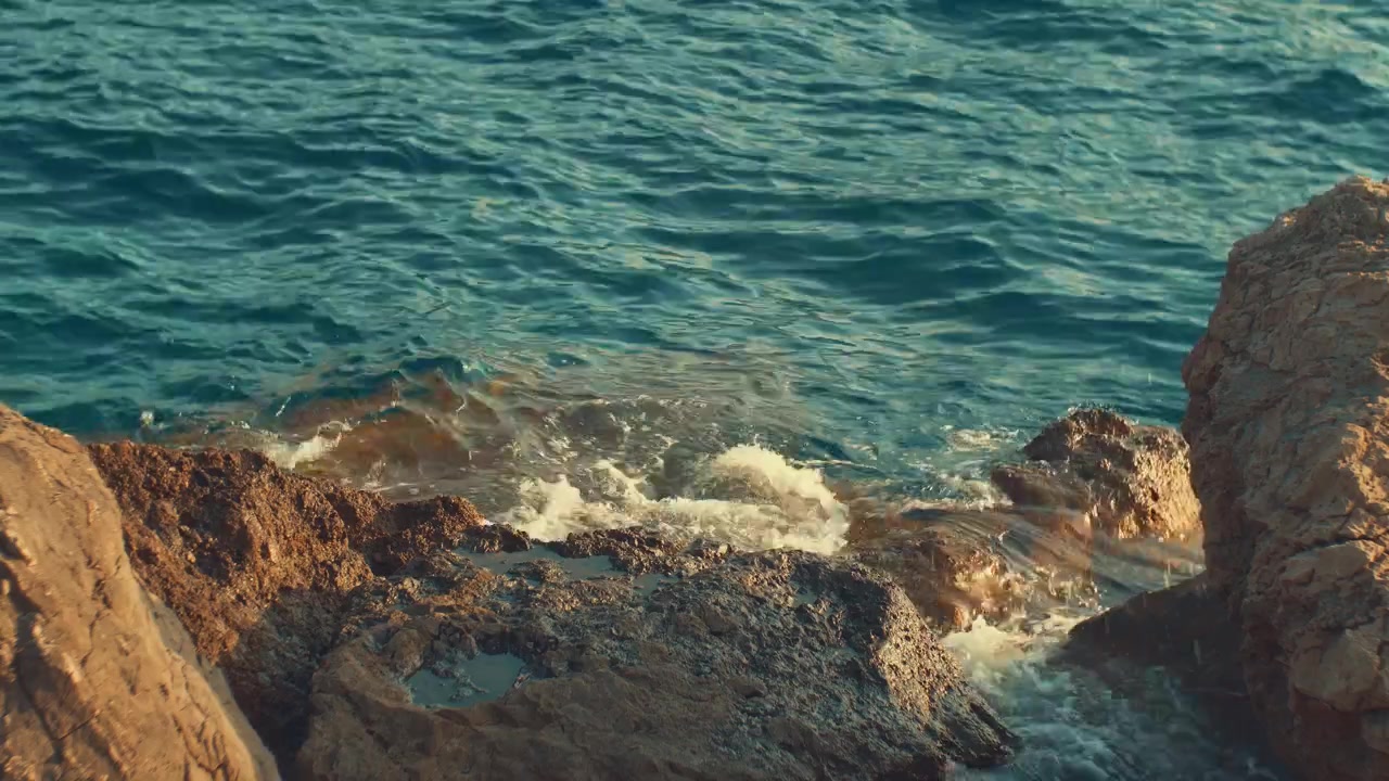 Primo piano di acqua di mare turchese trasparente che lambisce una spiaggia di ciottoli, creando delicati riflessi di luce e increspature