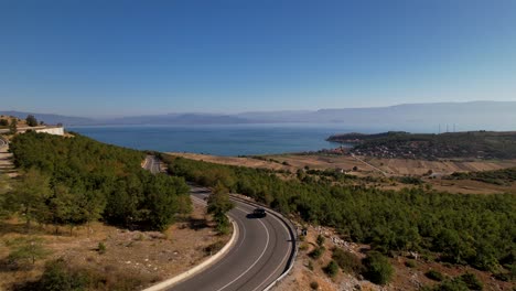 car drives on panoramic winding road near blue lake and panoramic coast of touristic village in albania