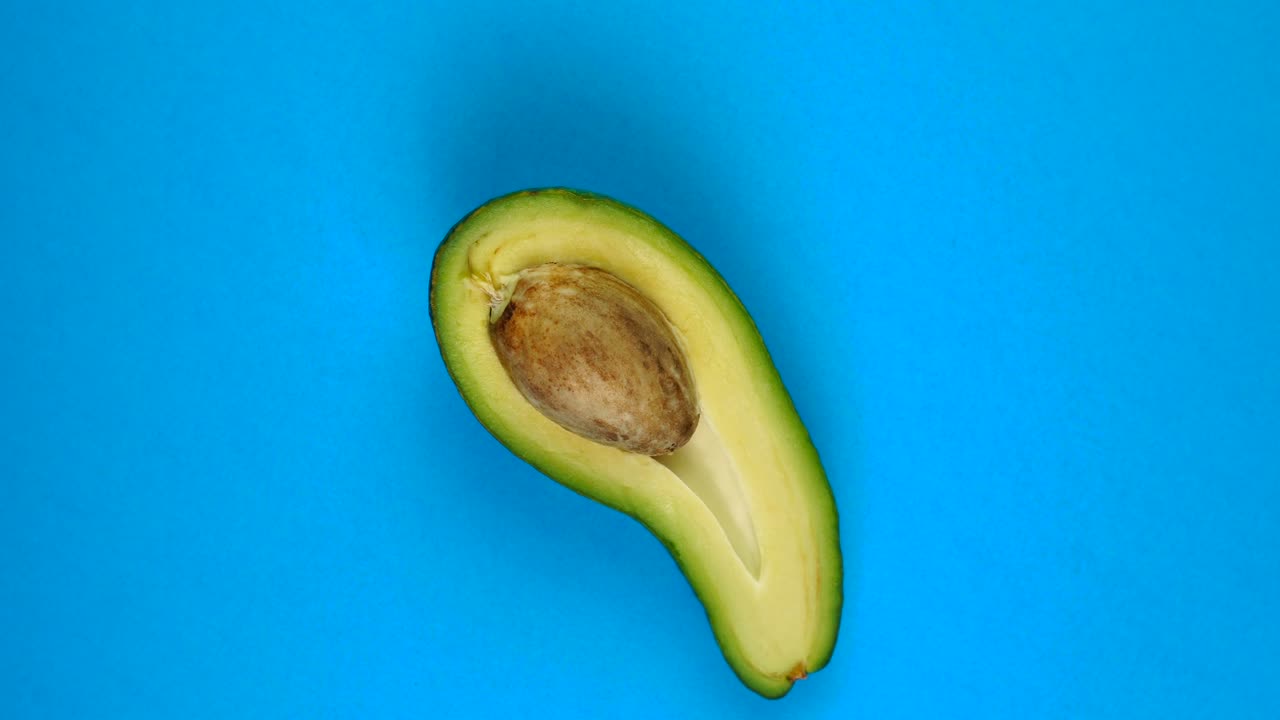 Mezzo avocado che ruota su un tavolo blu. L'avocado è un frutto altamente nutriente. Filmato in loop