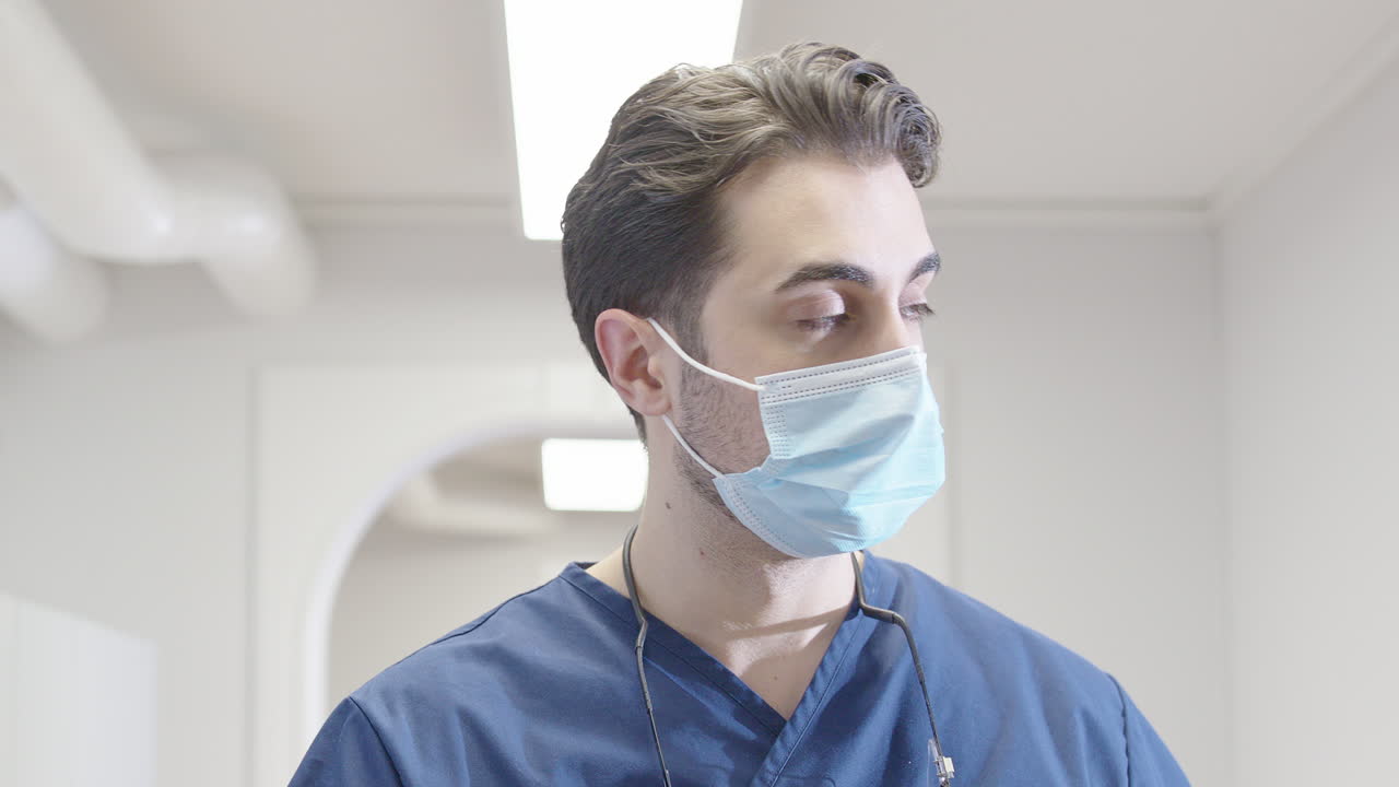 Male doctor with face mask walks down bright corridor in hospital, gimbal