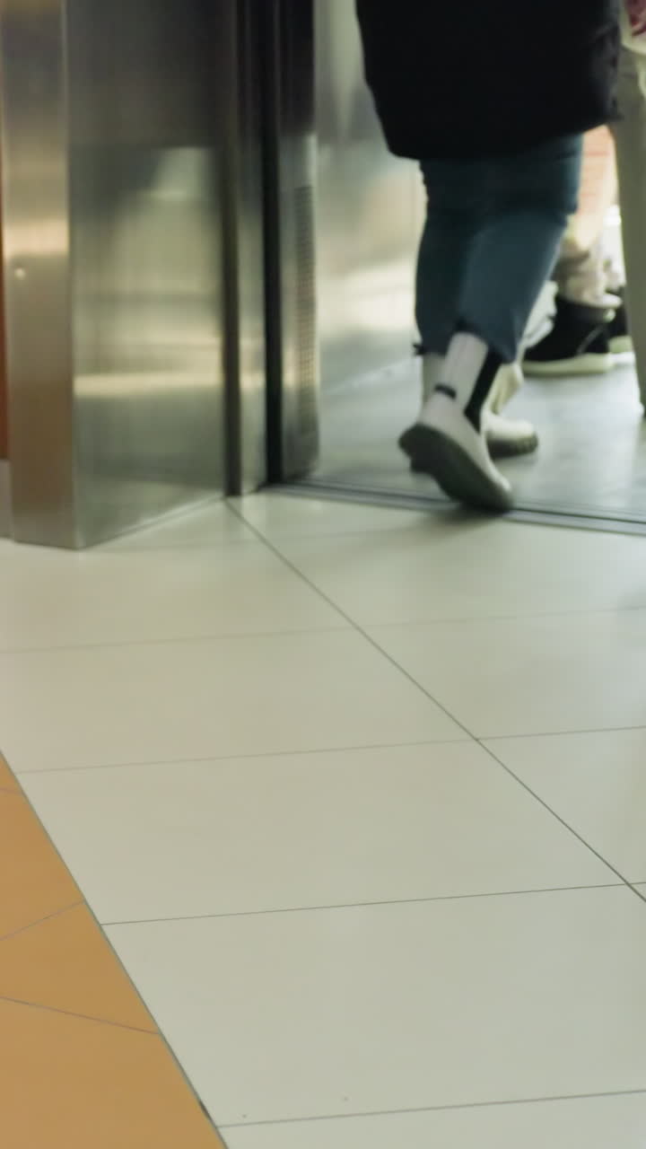 la mitad inferior de varias personas de pie y moviéndose dentro y fuera de un centro comercial. la imagen se centra en diferentes piernas y calzado, destacando un ambiente interior ocupado con diversos individuos