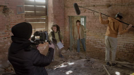 Vista-De-Cerca-De-Un-Camarógrafo-Grabando-Una-Escena-De-Una-Chica-Pelirroja-Huyendo-De-Un-Hombre-En-Un-Pasamontañas-Negro-En-Un-Edificio-En-Ruinas