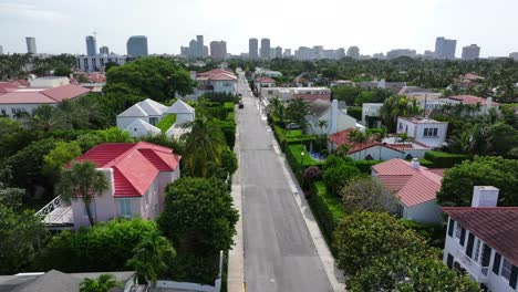 Drone-footage-of-a-residential-neighborhood-in-West-Palm-Beach,-featuring-tree-lined-streets,-Mediterranean-style-homes-with-red-and-white-roofs,-and-a-distant-city-skyline