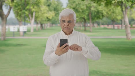 Un-Anciano-Indio-Serio-Desplazándose-Por-El-Teléfono-En-El-Parque