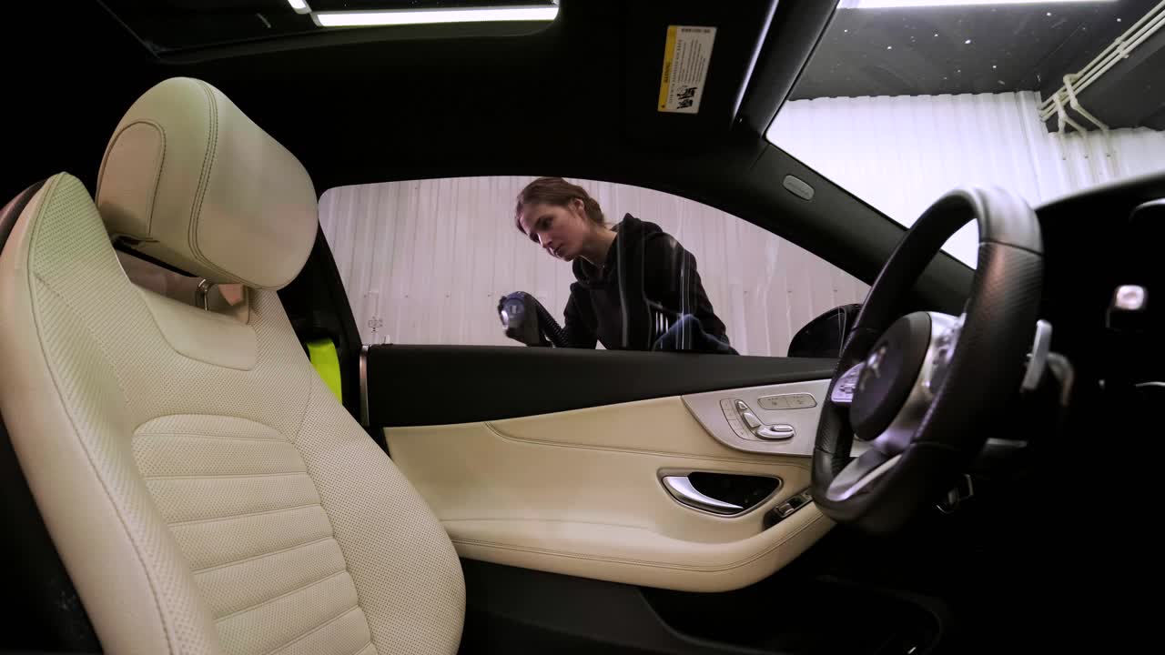 una mujer soplando agua de un coche negro recién lavado con aire.