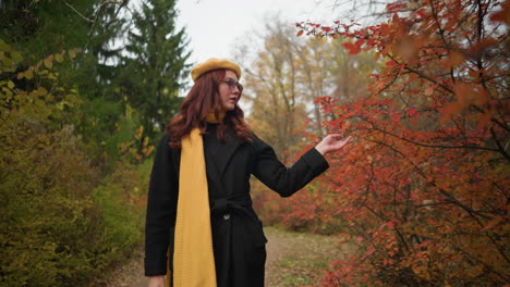 elegant lady in yellow beret and muffler explores autumn path, delicately touching vibrant red leaves, embodying the essence of fall's serene beauty