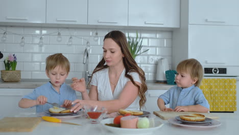 mom with two children in the kitchen at the table preparing burger for lunch