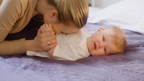 Close-Up-Of-A-Happy-Mother-Cuddling-And-Playing-With-Her-Baby-Boy-On-The-Bed-At-Home