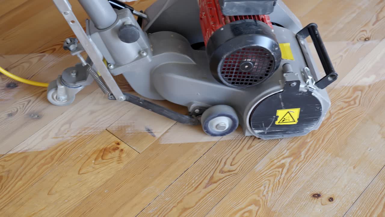 Floor sander in operation leaving trail of cleaned surface on dusty old wooden flooring
