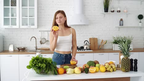 a woman cuts and sniffs a fresh orange with a knife. vegetarian food. white modern kitchen with vegetables and fruits
