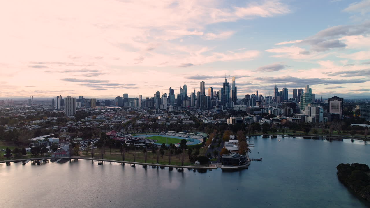 Smooth aerial perspective approach over Albert Park Lake toward Melbourne CBD.