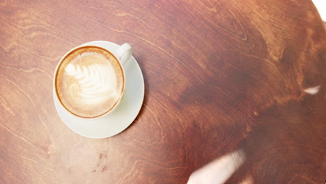 a cup of coffee with latte art sits on a wooden table in a cafe with copy space