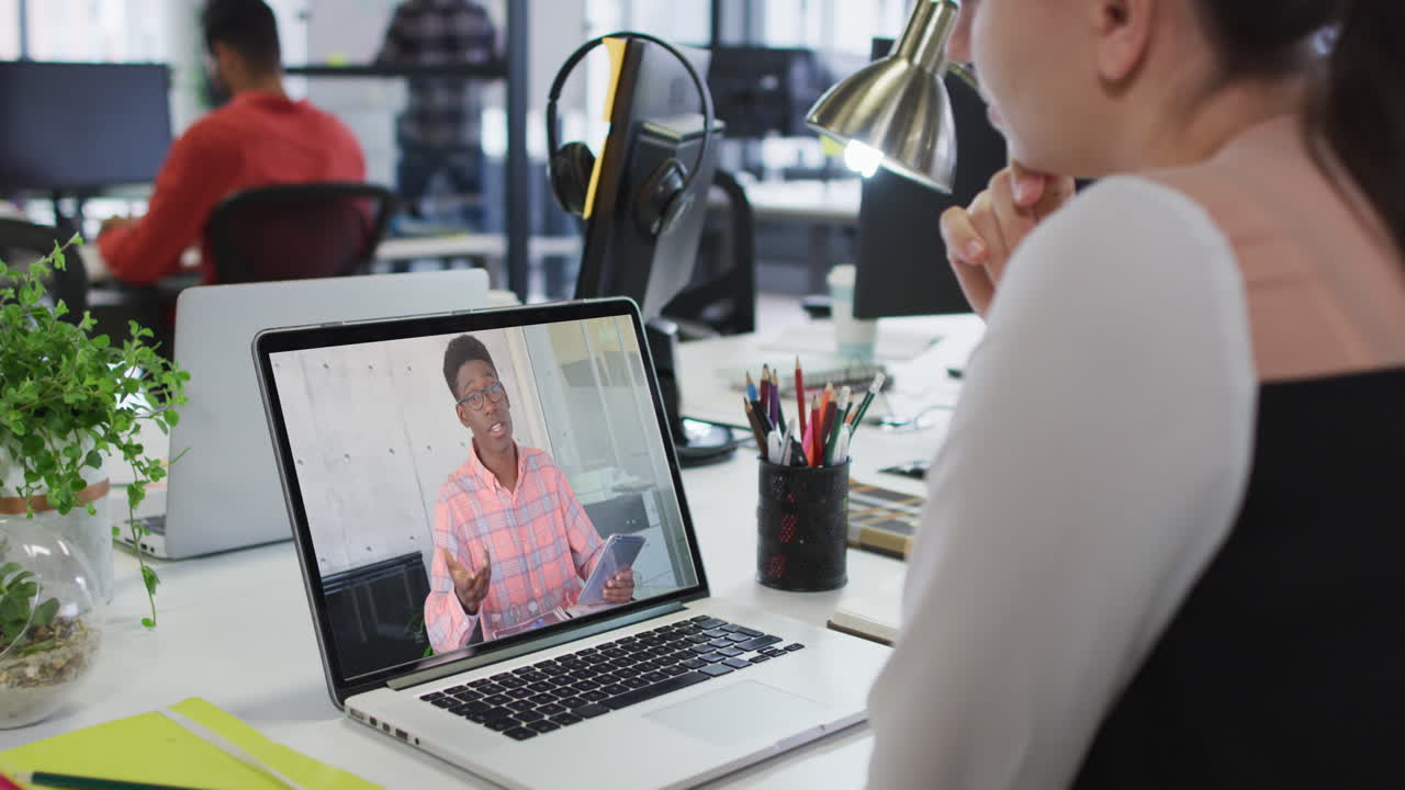 Caucasian woman having a video call on laptop with male colleague at office