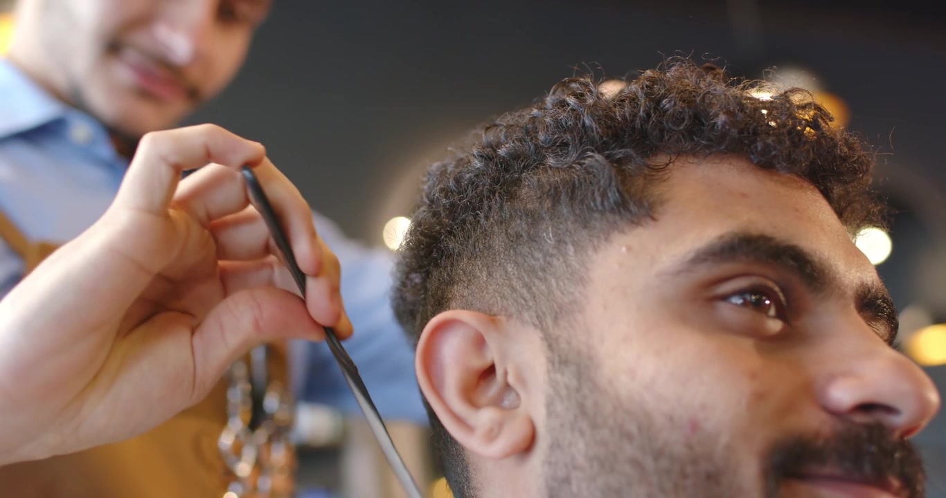 Barbiere con grembiule marrone che taglia i capelli a un cliente uomo afroamericano con un pettine nero, perfezionando la sfumatura in un salone