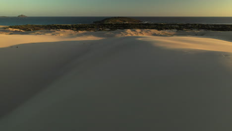 drone shot of man running on top of sand dune at the dark point sand dunes at hawks nest, new south wales, australia