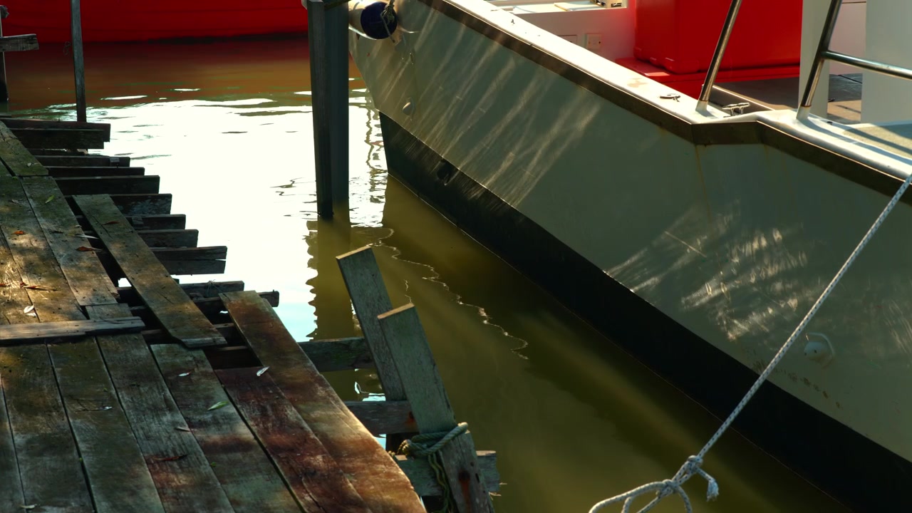 Boat hull docked alongside a weathered wooden jetty at day, water rippling in lake.