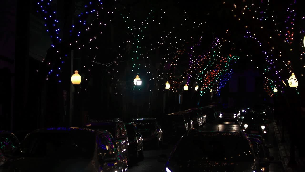 Various cars driving at night through downtown city streets with decorated trees for christmas festive season bright colorful lights Madeira Island celebrating xmas graded reveal tilt HD background