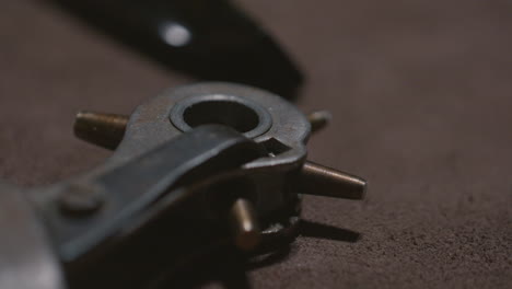detailed view of a metal rotary hole punch tool used for leatherworking, resting on a textured brown surface.