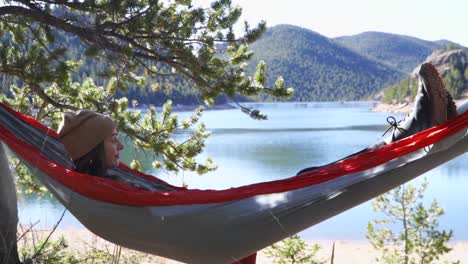 Young-brunette-woman-wearing-beanie-relaxes-in-hammock-by-reservoir