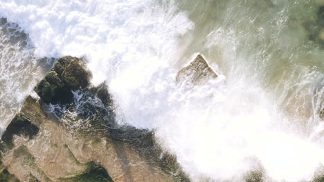 White-waves-rolling-up-onto-seaweed-covered-horizontal-bedded-sedimentary-ocean-rocks-aerial-view-panning-left-to-right-of-screen-Turimetta-Beach-Sydney-Australia