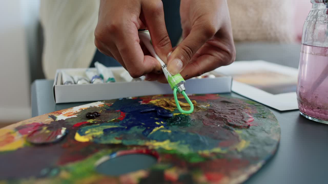 African American woman at home twisting cap, squeezing green paint tube onto palette, mixing