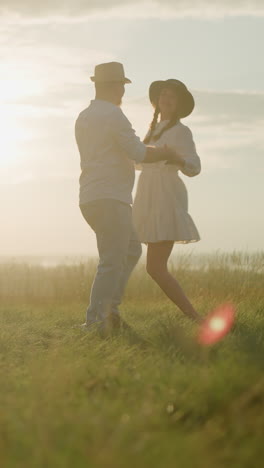 dos compañeros bailan alegremente en una colina cubierta de hierba iluminada por el sol al lado de un lago pacífico. el hombre, vestido con una camisa blanca, sombrero y vaqueros, comparte un momento tierno con su esposa, que lleva un vestido blanco