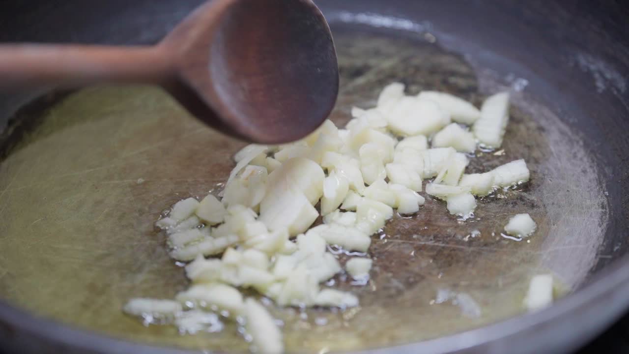 Primo piano di aglio tritato che cuoce in olio caldo e viene mescolato con un cucchiaio di legno