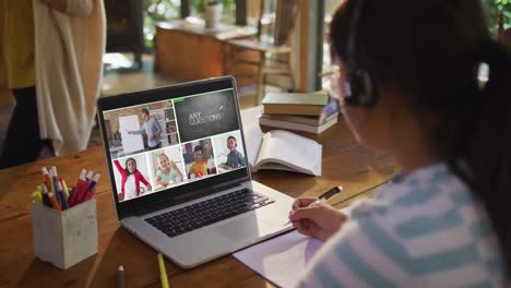 schoolgirl using laptop for online lesson at home, with diverse teacher and class on screen