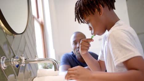padre y hijo afroamericanos cepillándose los dientes en el baño en casa, en cámara lenta