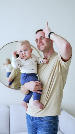 proud caucasian father with his adorable baby boy. dad and son holding his hands up together. mirror at backdrop. vertical video.
