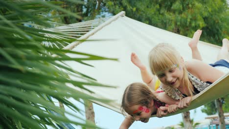 two cool girls with aquagrim on the face have fun, play a hammock on the territory of the tourist hotel