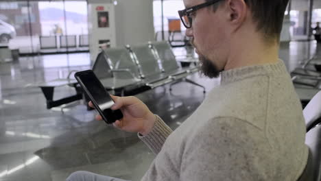 man using smartphone in airport waiting area