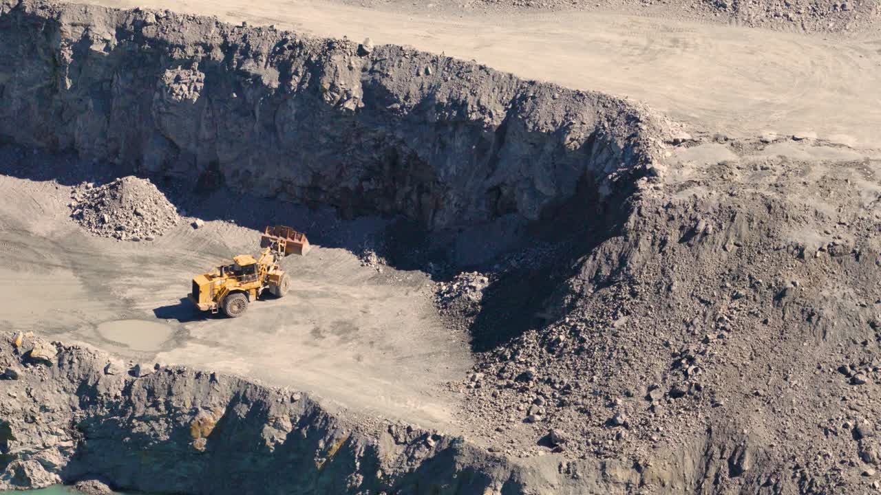 Drone footage captures excavators and trucks in a quarry, highlighting industrial activity and rugged terrain under bright daylight