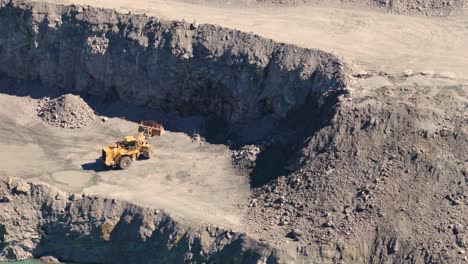 drone footage captures excavators and trucks in a quarry, highlighting industrial activity and rugged terrain under bright daylight