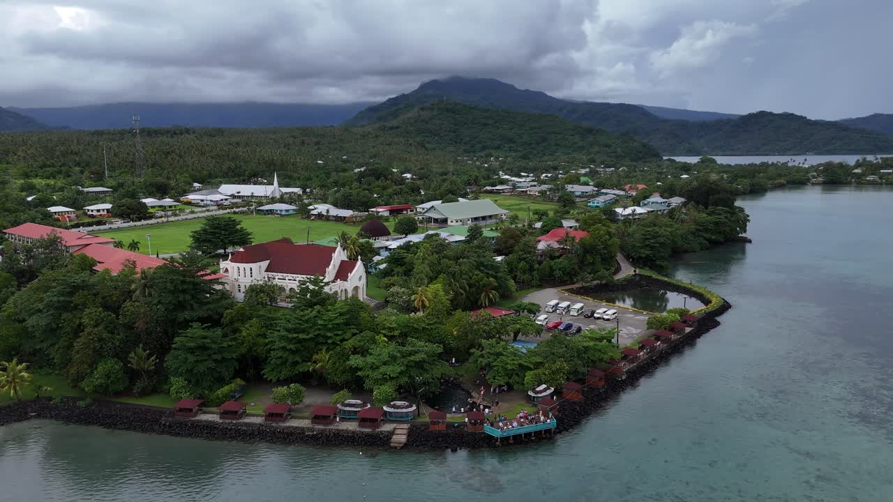 Vista aerea mozzafiato di un pacifico villaggio costiero delle Samoa, con architettura tradizionale immersa tra la rigogliosa vegetazione tropicale e le acque blu dell'Oceano Pacifico