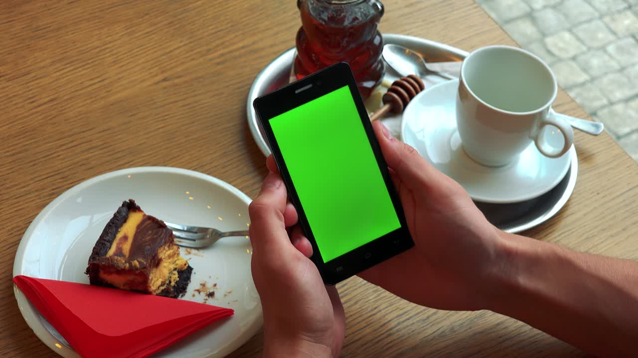 un hombre sostiene un teléfono inteligente con una pantalla verde sobre una mesa con comida - primer plano desde arriba en el teléfono inteligente