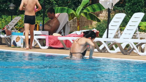 people sitting by the poolside of a resort swimming pool during summer holiday