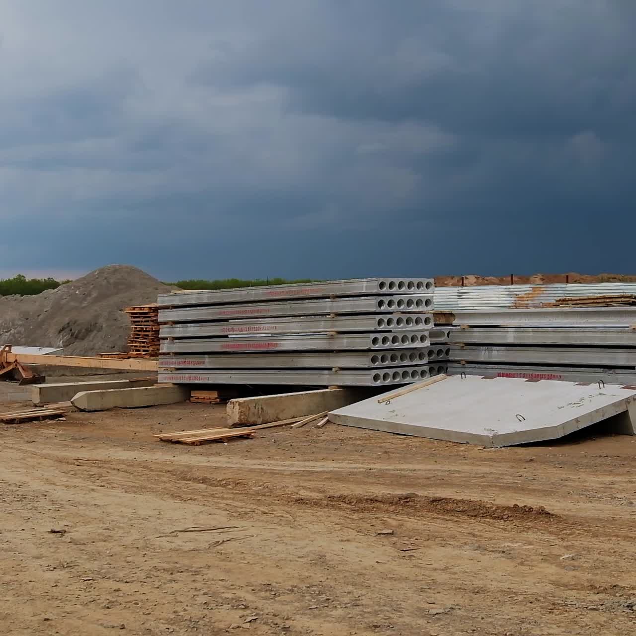 Long grey concrete blocks stacked outdoors. Piles of spalls near the metal fence. Grey dramatic sky t backdrop