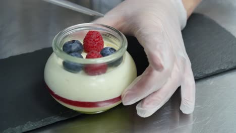 chef preparing layered dessert in glass jars with raspberries and blueberries