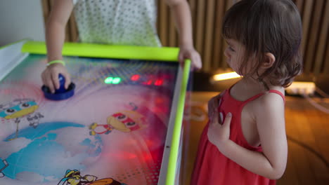 cute concentrated little girl watching how older children playing air hockey table game indoors