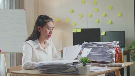 tired asian woman shaking her head while working hard with documents at the office