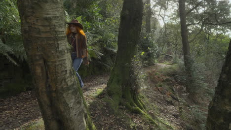 Redheaded-women-walking-from-behind-tree-along-shady-English-woodland-path
