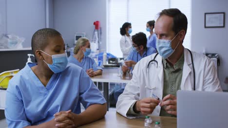 Diverse-male-and-female-doctor-talking,-man-preparing-covid-vaccination,-both-wearing-face-masks