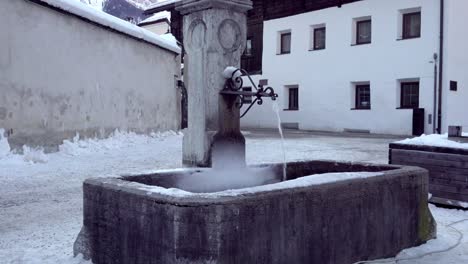 La-Fuente-Del-Pueblo-En-Invierno-Con-Agua-Corriente-Y-Una-Ligera-Capa-De-Nieve-En-El-Centro-De-La-Ciudad-De-Innichen---San-Candido,-Tirol-Del-Sur,-Italia