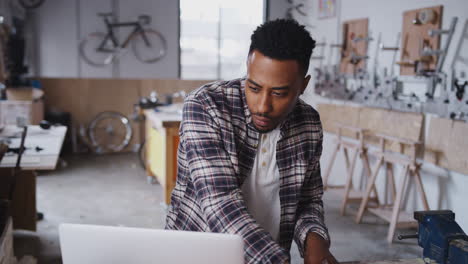 Young Male Business Owner In Workshop For Sustainable Bicycles Doing Accounts On Laptop