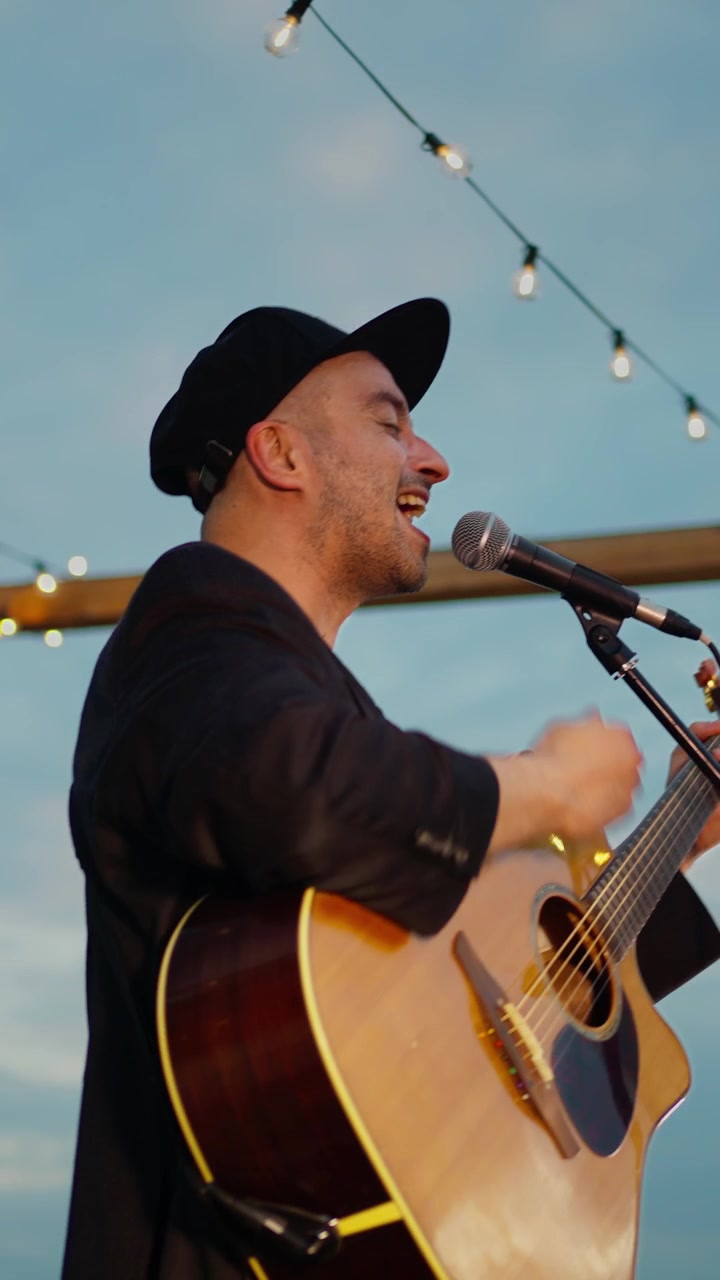 Musiker spiller akustisk guitar og synger til et udendørs aftenarrangement