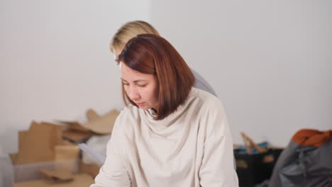 seamstress arranging sewing materials while discussing colorful fabric samples with colleague in bright workshop, showing teamwork and preparation process, mannequin and folded fabrics