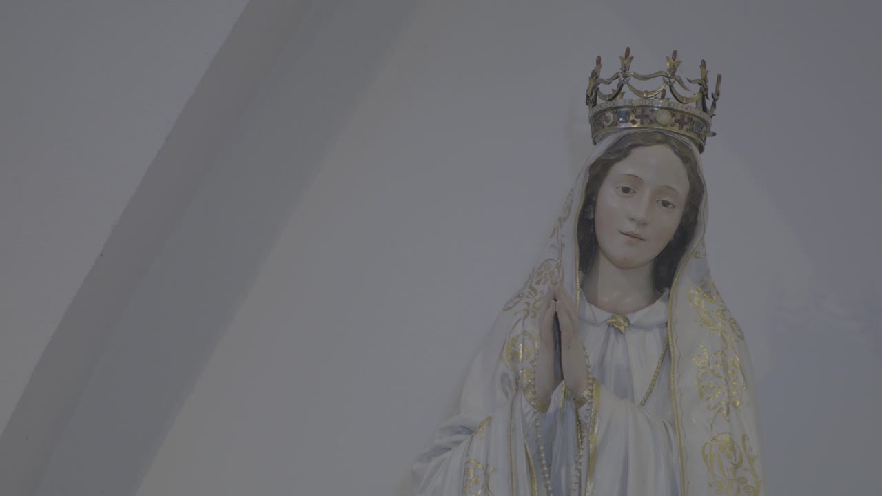 Camera pans to a statue of Mother Mary with folded hands