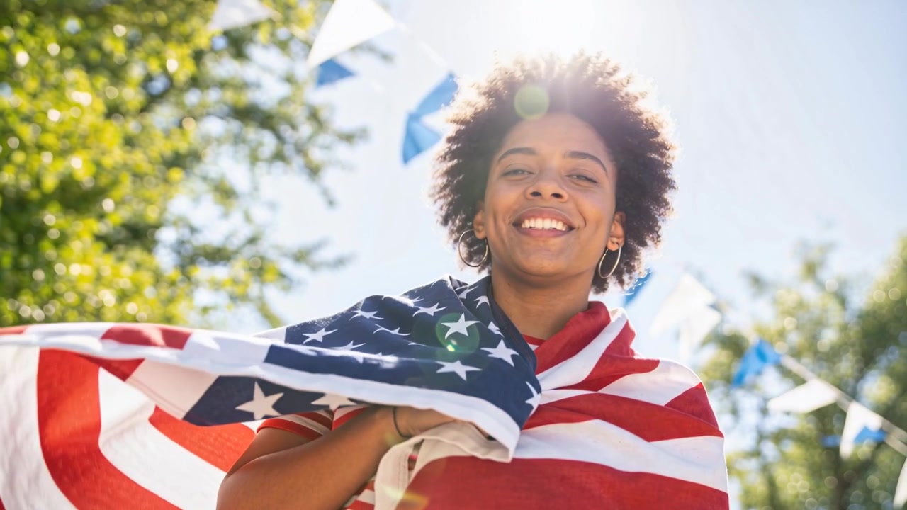 Riprese in corso, donna avvolta nella bandiera americana che festeggia e sistema la bandiera al parco, con una maglietta a righe.